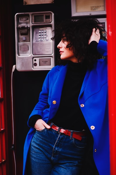 一个穿着蓝色皮衣靠在电话亭上的女人